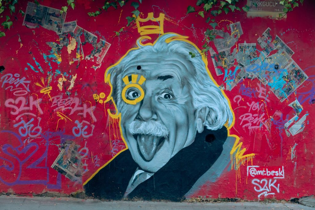 Street art mural on a red wall showing a white-haired scientist sticking out his tongue