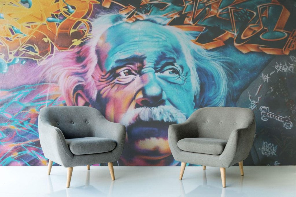 Two gray armchairs placed in front of a colorful street art mural of a scientist