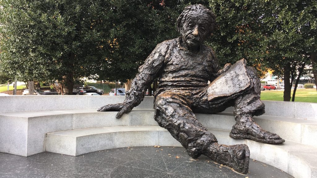 Outdoor sculpture of a seated scientist holding a book on stone steps