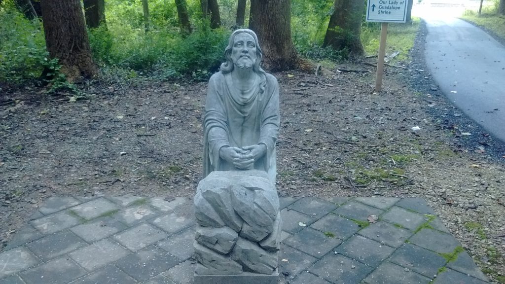 A statue of Jesus praying in a forest setting